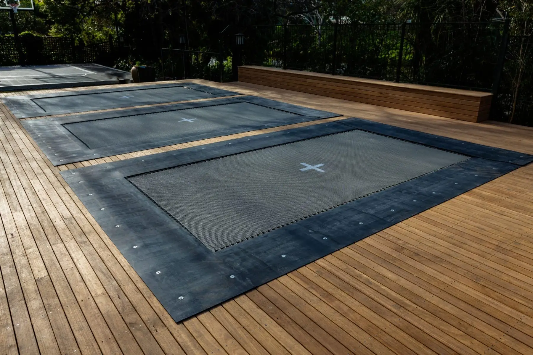 Three deck-mounted Mr Trampolines set flush into a large timber deck, with charcoal mats and black rubber surrounds