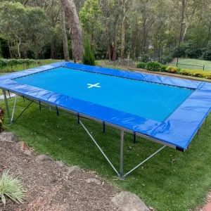 Above-ground Mr Trampoline with blue padded surrounds on galvanised legs, on a lawn in a bush garden at Park Orchards