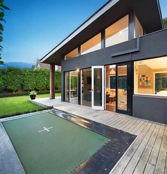 Deck-mounted Mr Trampoline with a dark green mat set flush into a timber deck beside a modern home