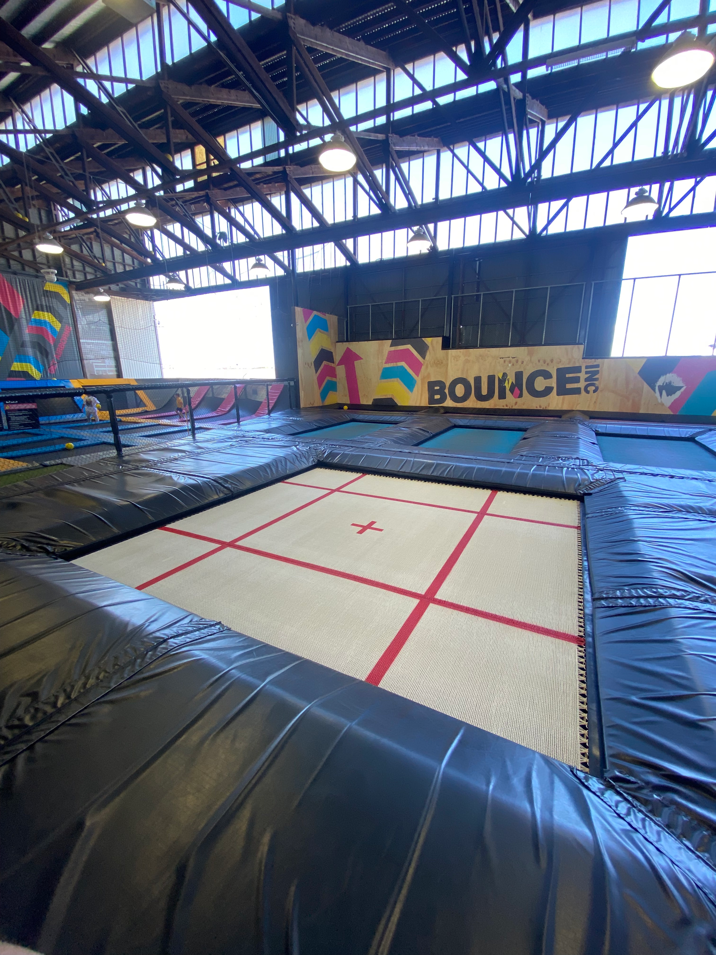Large indoor performance bed with red cross markings and a black padded surround in a commercial trampoline venue